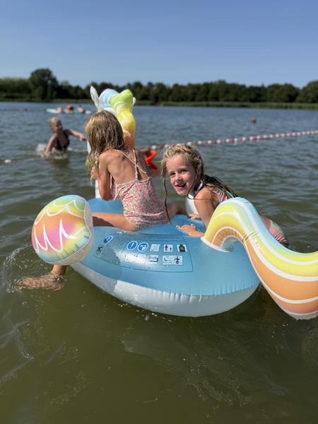 Two young girls play on an inflatable boat in a lake on a sunny day